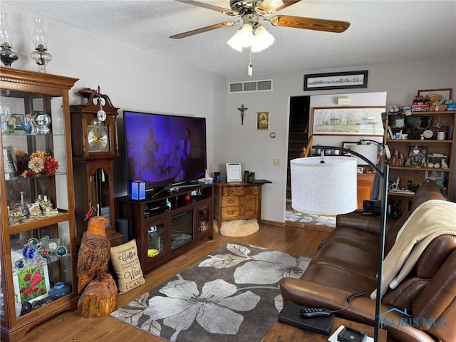 living room with hardwood / wood-style flooring, ceiling fan, and a textured ceiling