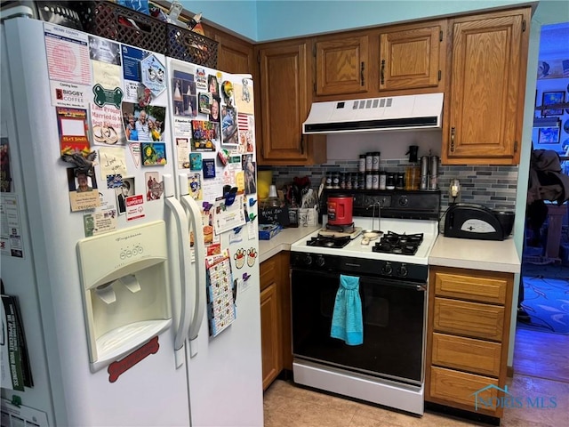 kitchen featuring tasteful backsplash, range with gas stovetop, and white refrigerator with ice dispenser