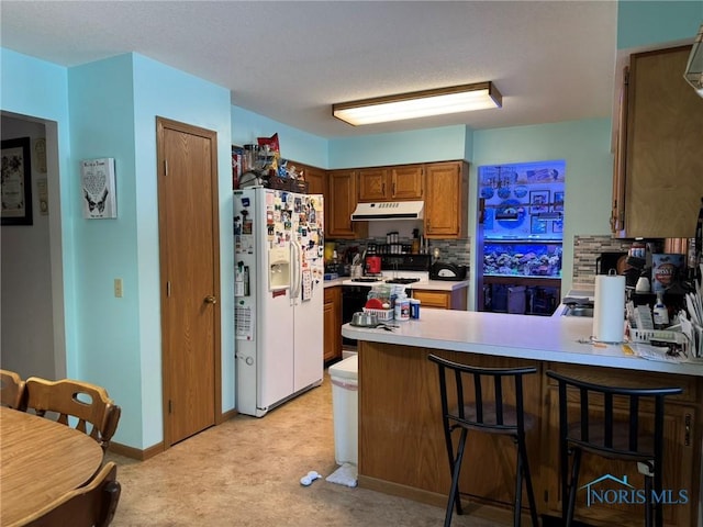 kitchen featuring a kitchen bar, white refrigerator with ice dispenser, gas stove, and kitchen peninsula