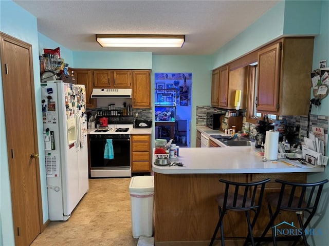 kitchen with a kitchen bar, sink, range with gas stovetop, kitchen peninsula, and white refrigerator with ice dispenser