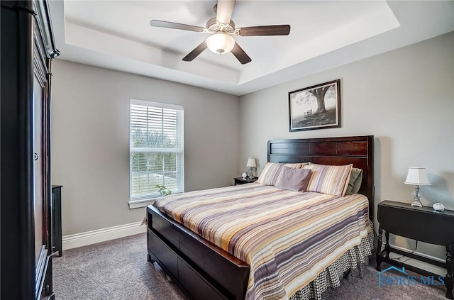 carpeted bedroom with a raised ceiling and ceiling fan