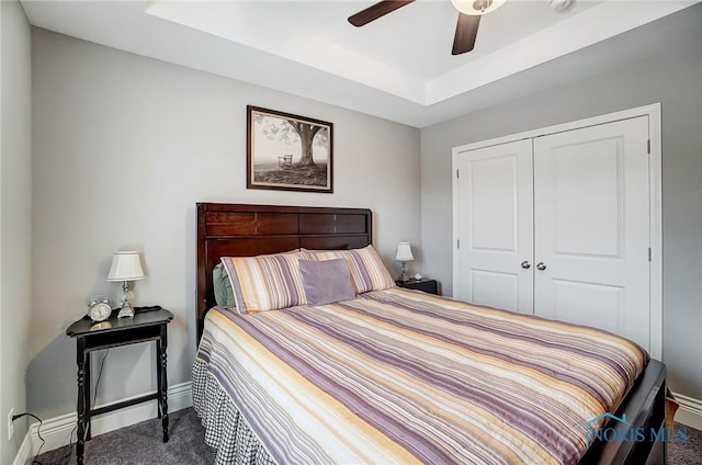 bedroom with ceiling fan, a tray ceiling, carpet flooring, and a closet