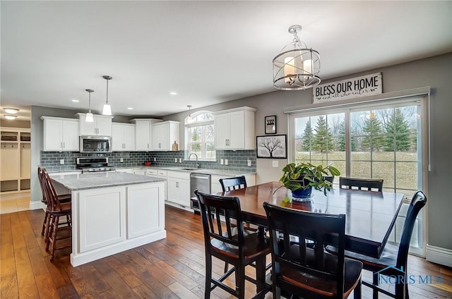 kitchen featuring appliances with stainless steel finishes, a kitchen island, white cabinetry, hanging light fixtures, and dark wood-type flooring