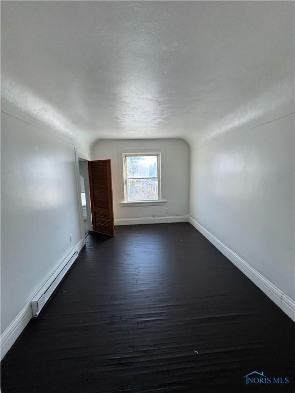 unfurnished room featuring lofted ceiling, dark wood-type flooring, a baseboard radiator, and a textured ceiling