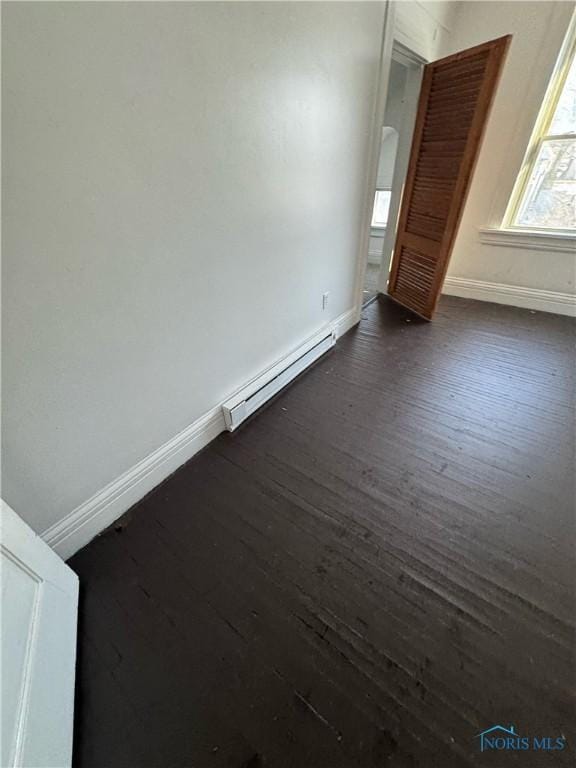 unfurnished room with a baseboard heating unit and dark wood-type flooring