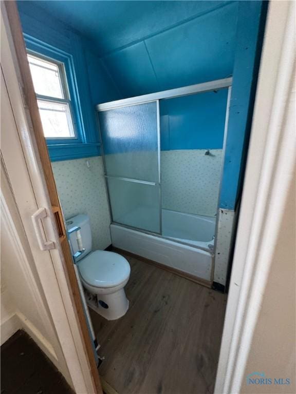 bathroom with hardwood / wood-style flooring, bath / shower combo with glass door, and toilet