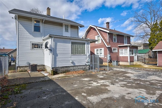 rear view of house with entry steps, driveway, central AC unit, a chimney, and fence