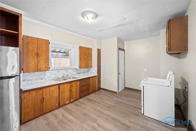 kitchen with washer / dryer, sink, light hardwood / wood-style flooring, stainless steel fridge, and backsplash