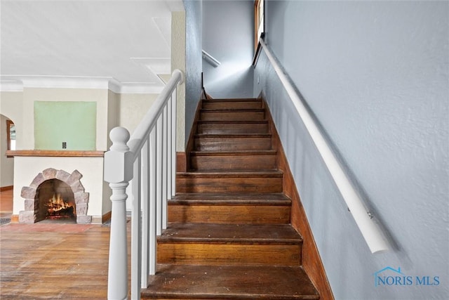 staircase featuring a brick fireplace, crown molding, and hardwood / wood-style floors