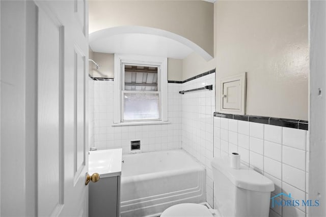 full bathroom featuring tiled shower / bath combo, vanity, tile walls, and toilet