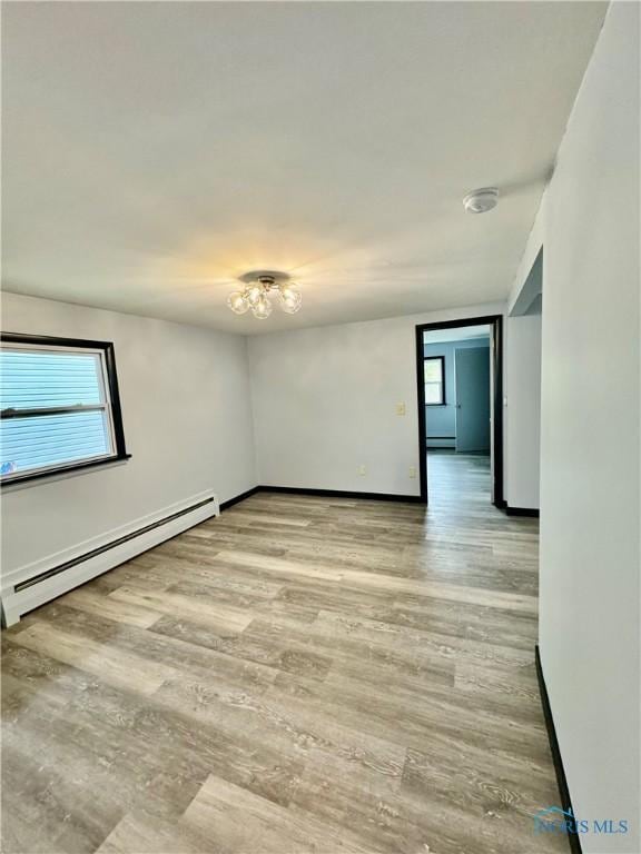 unfurnished room with baseboard heating, light hardwood / wood-style floors, and a wealth of natural light