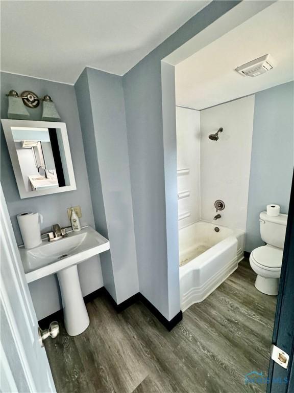 bathroom featuring hardwood / wood-style flooring, shower / washtub combination, and toilet