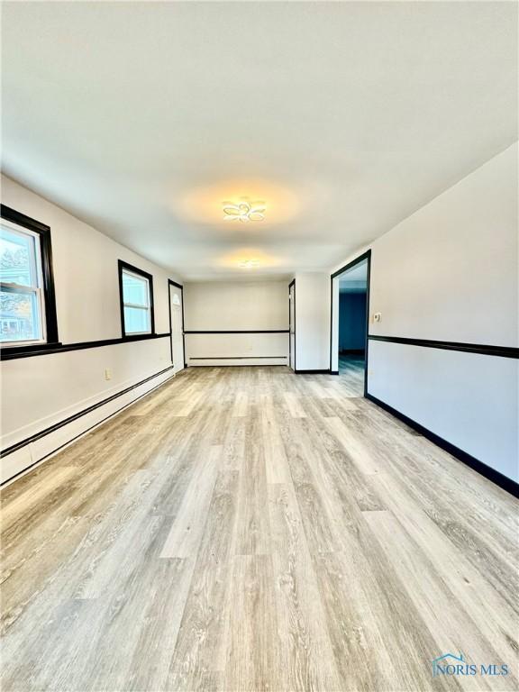 spare room featuring a baseboard heating unit and light hardwood / wood-style flooring