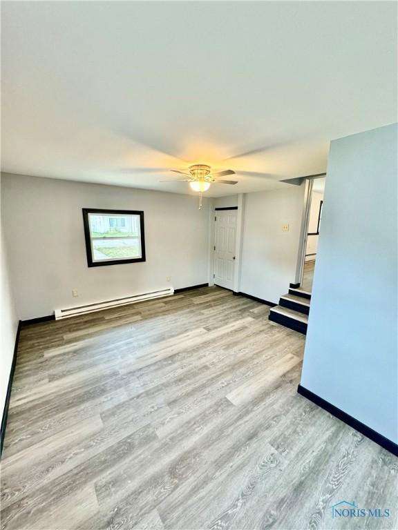 empty room featuring a baseboard radiator, ceiling fan, and light wood-type flooring