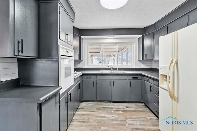 kitchen featuring white appliances, tasteful backsplash, light wood-style flooring, gray cabinets, and a sink