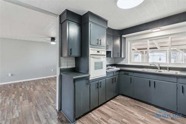 kitchen featuring a sink, baseboards, light wood-style floors, white oven, and backsplash