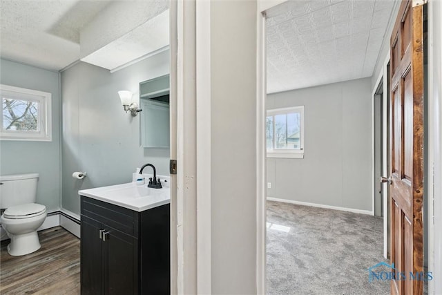 half bath with toilet, a baseboard heating unit, vanity, a textured ceiling, and baseboards