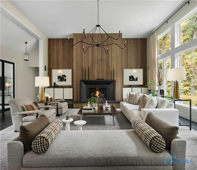 living room with an inviting chandelier, a healthy amount of sunlight, wooden walls, and vaulted ceiling