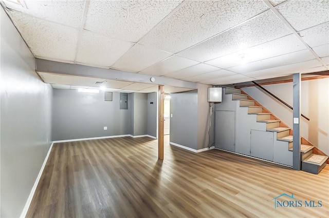 basement featuring a drop ceiling, wood-type flooring, and electric panel