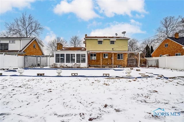 snow covered back of property featuring a sunroom