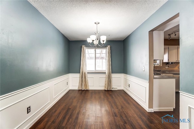 unfurnished dining area featuring dark hardwood / wood-style flooring, a chandelier, a textured ceiling, and rail lighting