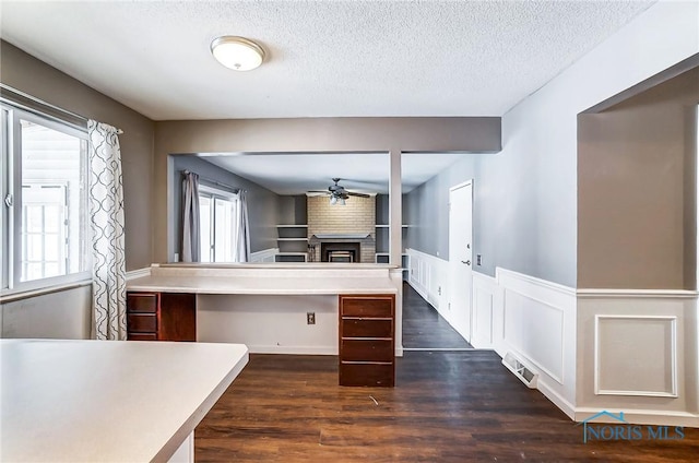 kitchen featuring ceiling fan, dark hardwood / wood-style flooring, a brick fireplace, and a textured ceiling