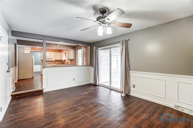 unfurnished living room featuring dark wood-type flooring and ceiling fan