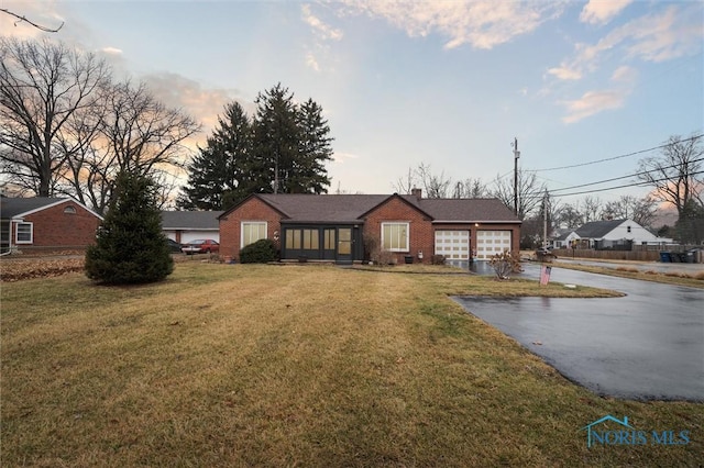 single story home featuring driveway, brick siding, an attached garage, and a yard