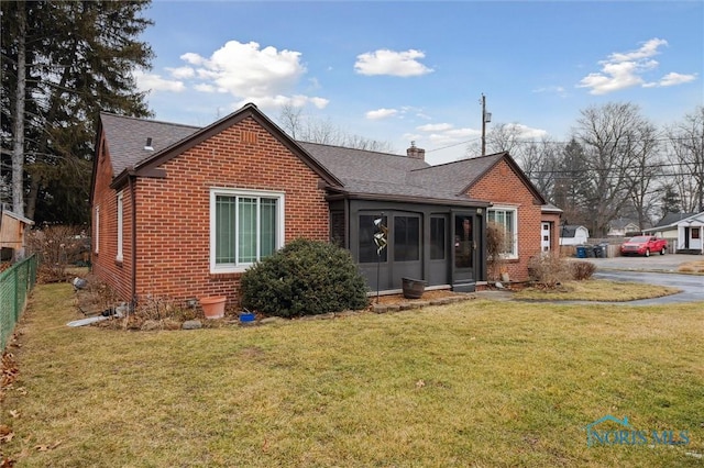 view of front of home with brick siding, fence, a sunroom, a front lawn, and a chimney