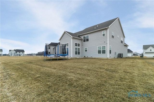 rear view of property featuring a trampoline, central AC unit, and a lawn