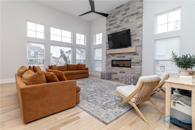 living room with ceiling fan, a towering ceiling, a fireplace, and light hardwood / wood-style floors