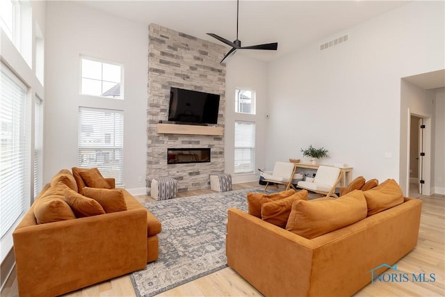 living room featuring a stone fireplace, plenty of natural light, light hardwood / wood-style floors, and ceiling fan