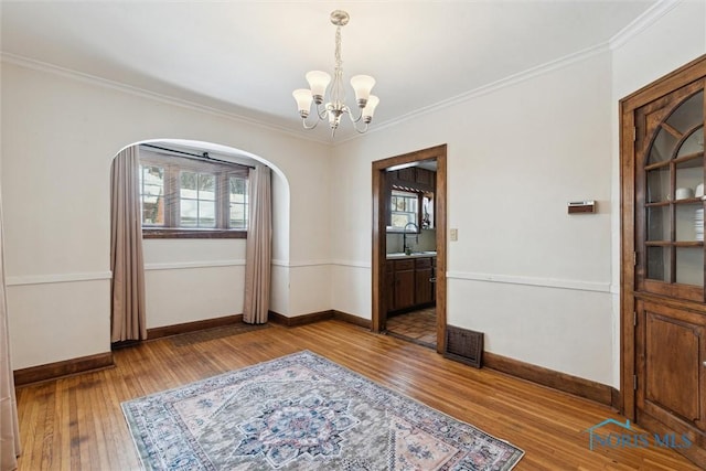 empty room with wood finished floors, a notable chandelier, a healthy amount of sunlight, and arched walkways