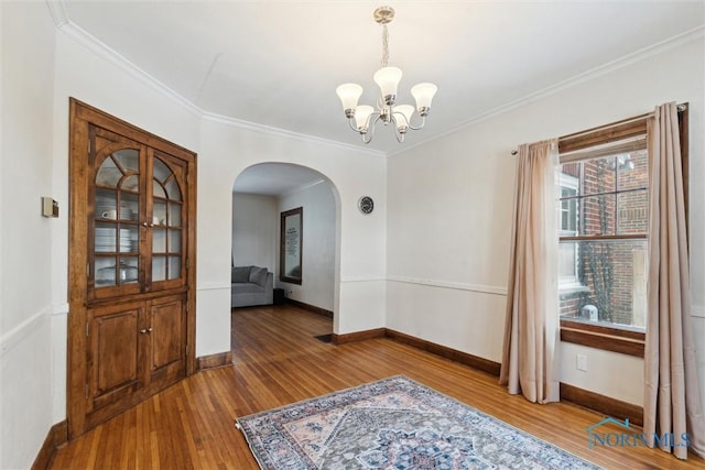 interior space featuring a chandelier, ornamental molding, arched walkways, and wood finished floors