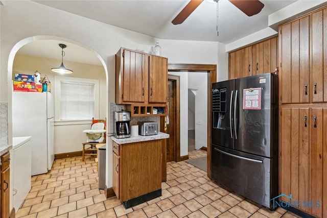kitchen featuring brown cabinetry, black fridge with ice dispenser, and freestanding refrigerator
