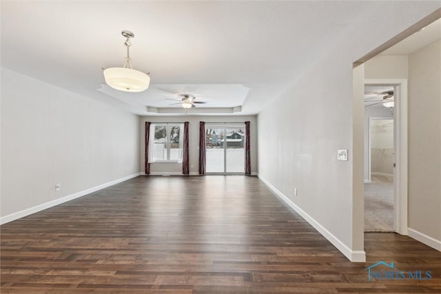 unfurnished room with a ceiling fan, a raised ceiling, dark wood finished floors, and baseboards