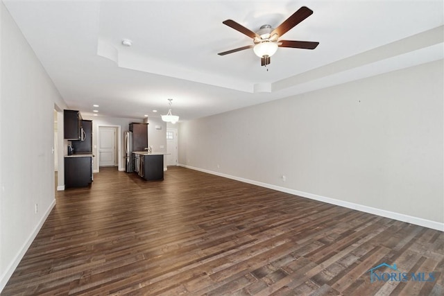 unfurnished living room featuring a tray ceiling, dark wood finished floors, recessed lighting, a ceiling fan, and baseboards