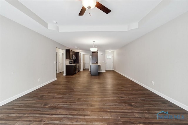 unfurnished living room with dark wood-style floors, ceiling fan, a tray ceiling, and baseboards