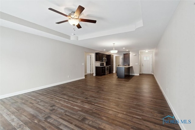 unfurnished living room featuring a ceiling fan, dark wood-style flooring, a raised ceiling, and baseboards