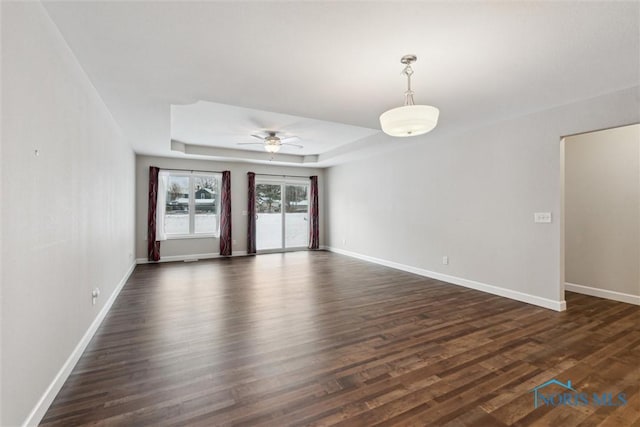 empty room with ceiling fan, a tray ceiling, dark wood-type flooring, and baseboards