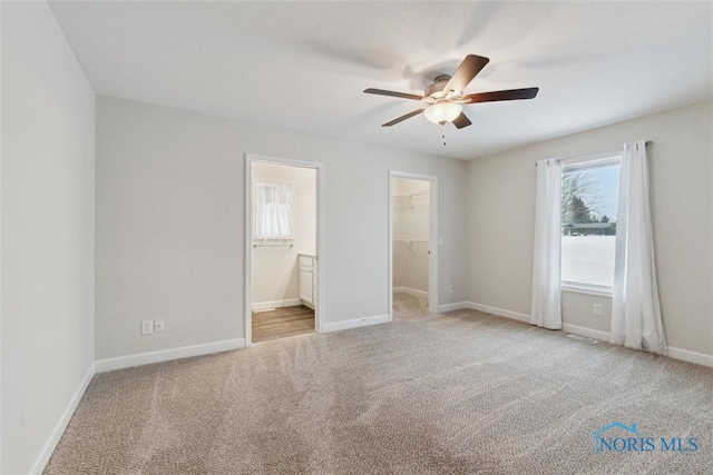 unfurnished bedroom with light carpet, a spacious closet, baseboards, and ensuite bathroom