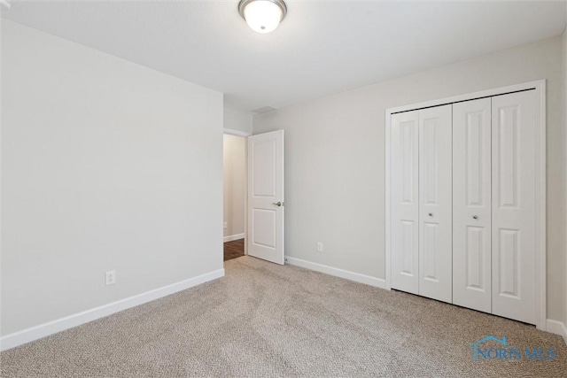 unfurnished bedroom featuring light carpet, baseboards, and a closet