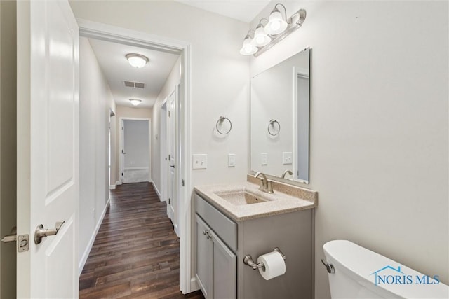 bathroom featuring toilet, wood finished floors, vanity, visible vents, and baseboards