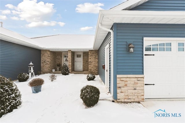 snow covered property entrance with a garage and stone siding