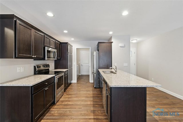 kitchen featuring stainless steel appliances, a sink, light wood finished floors, and light stone countertops