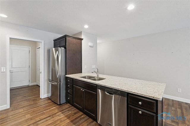 kitchen with appliances with stainless steel finishes, dark wood-type flooring, a sink, and light stone counters