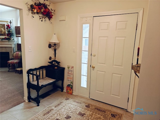 foyer entrance featuring light tile patterned floors, light colored carpet, and a fireplace