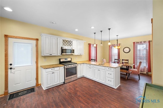 kitchen with dark wood-type flooring, appliances with stainless steel finishes, white cabinets, decorative light fixtures, and kitchen peninsula