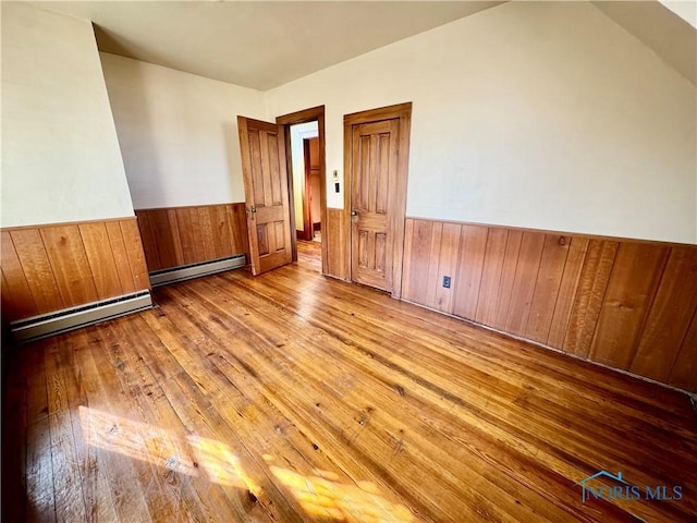 unfurnished room with a baseboard heating unit, wood walls, and light hardwood / wood-style flooring