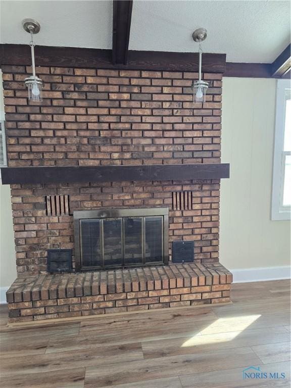 room details with beam ceiling, a brick fireplace, hardwood / wood-style flooring, and a textured ceiling